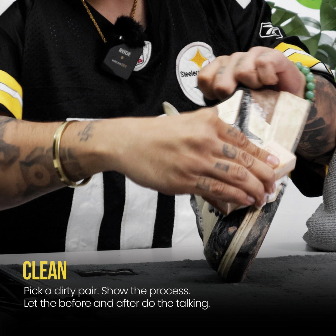 Person cleaning a shoe with a shoe brush, wearing a black sports jersey with yellow and white accents.
