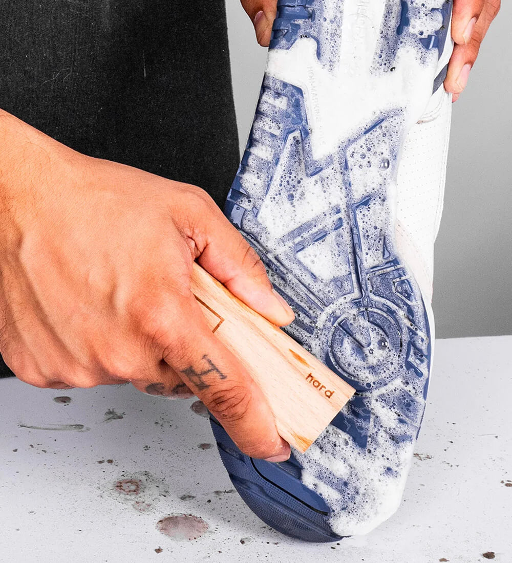 Person cleaning a blue and white sneaker outsole with the SHOEGR Hard Shoe Brush