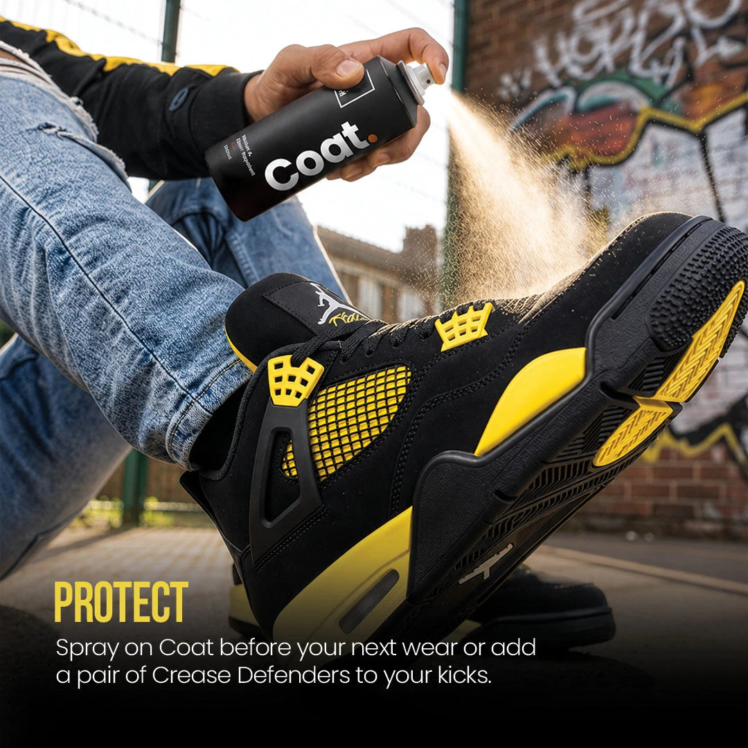 Person spraying a water proofing spray called SHOEGR Coat on a black and yellow sneaker with graffiti in the background.