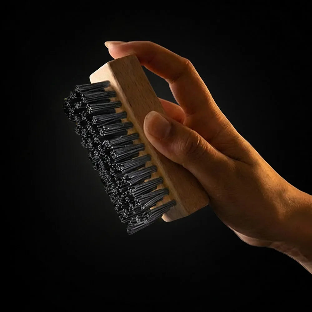 Hand holding the SHOEGR all-purpose shoe brush with black bristles against a dark background