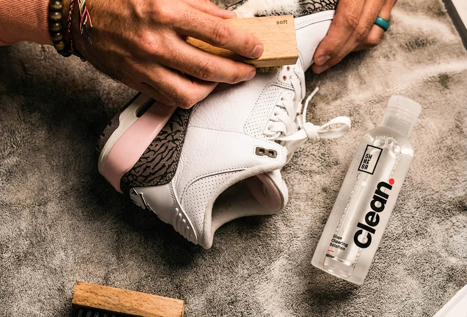 Person cleaning a white sneaker with the SHOEGR Ultimate Kit Soft Brush and Clean.