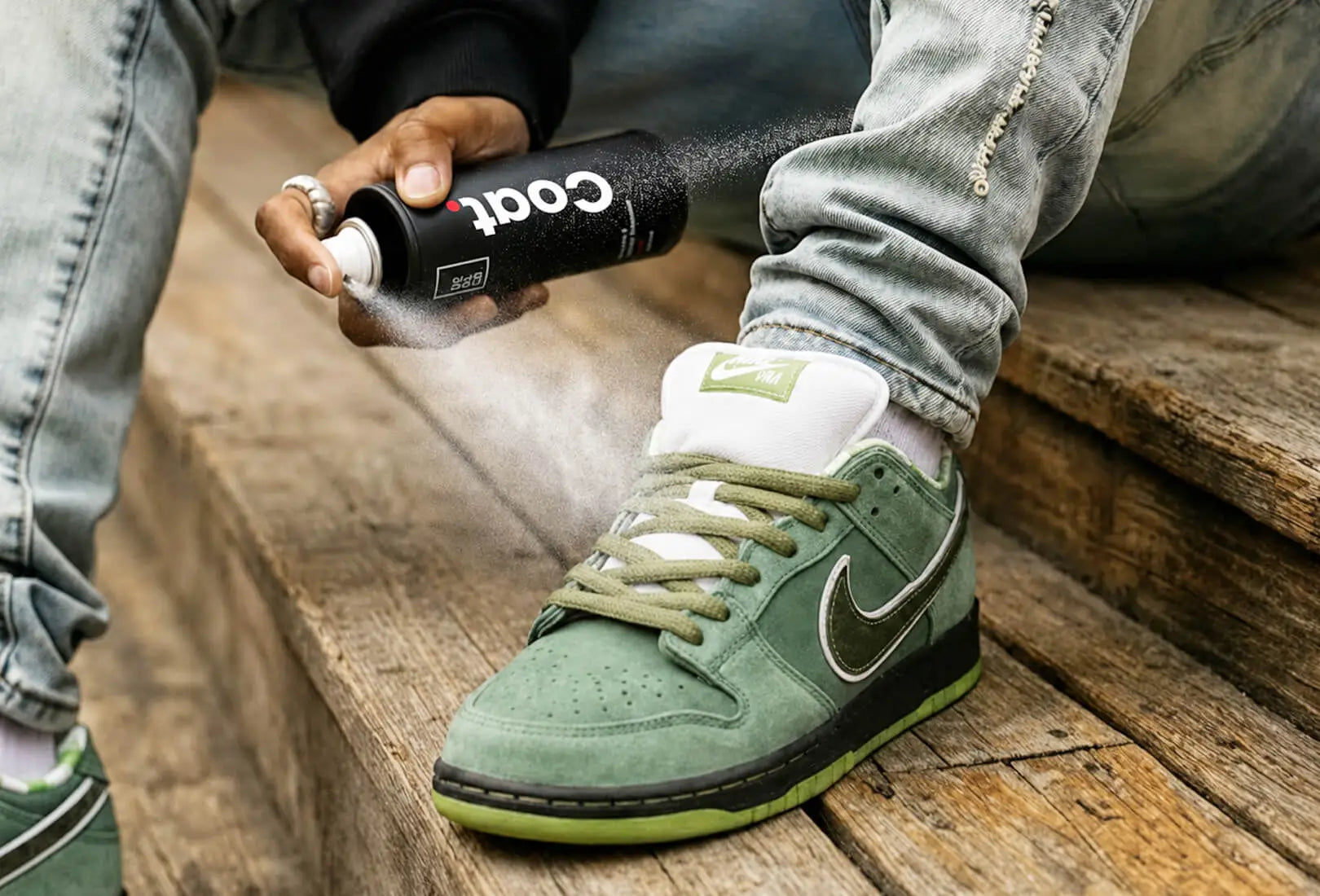 Person applying SHOEGR Coat water and stain repellent to a green nike sneaker