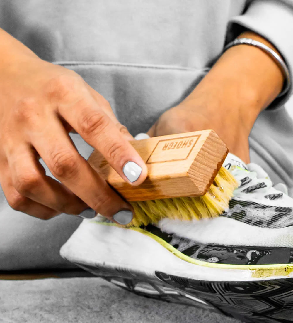 Person cleaning a black and white sneaker with SHOEGR Soft Brush